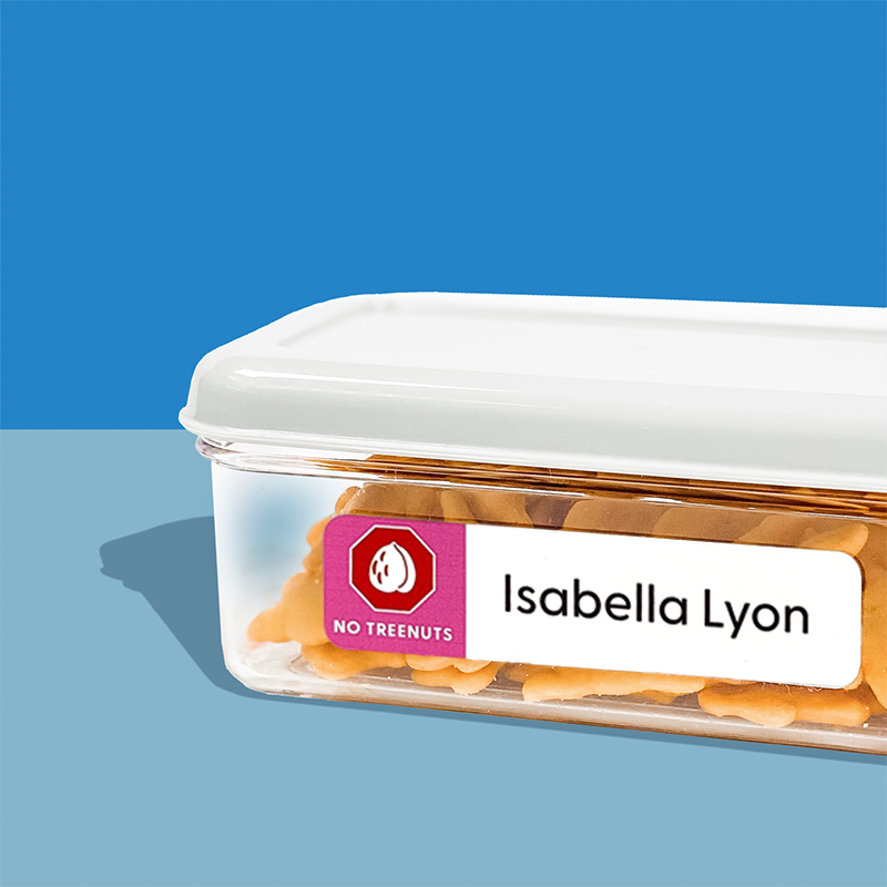 A clear plastic container with a white lid, labeled with an InchBug allergy alert name sticker label that reads 'Isabella Lyon' and has a red icon that indicates 'No Tree Nuts'. 