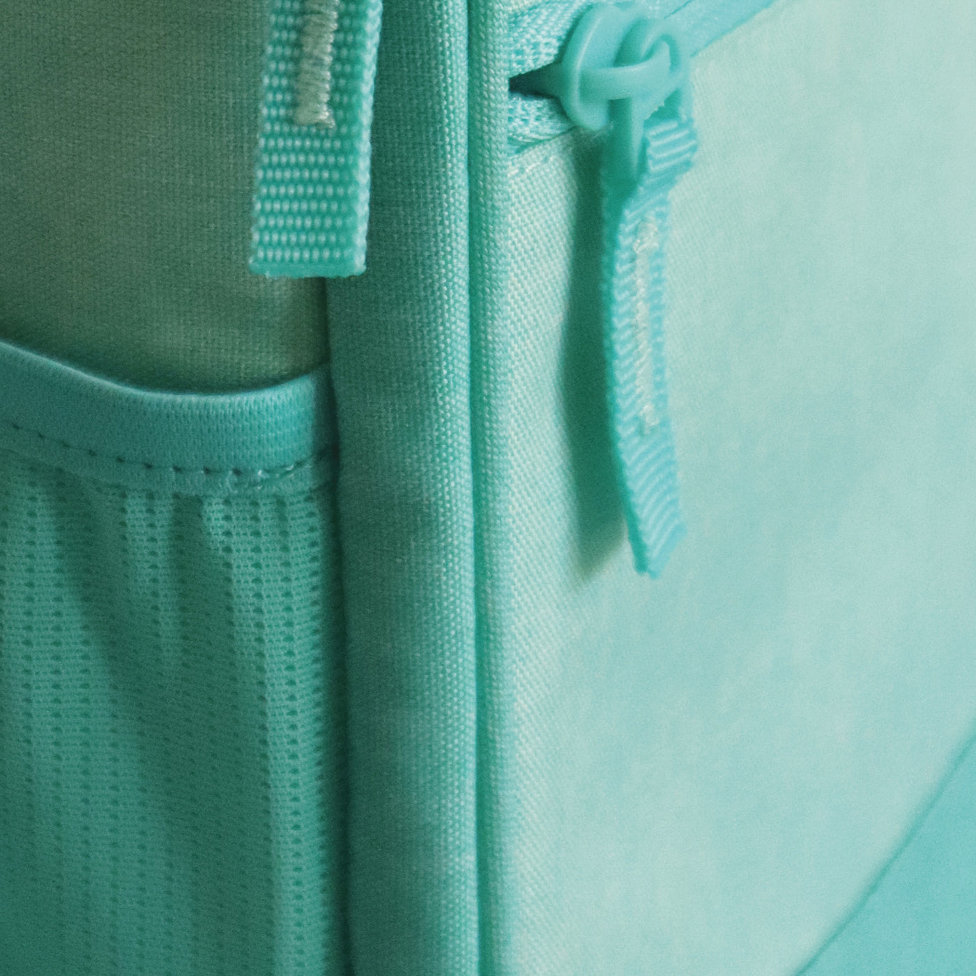 A blue backpack with an InchBug personalized circular kid's bag tag attached to it, placed against a two-tone background