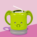 A green InchBug MyDrinky adjustable juice box holder with a cartoon face and sturdy handles, attached to a grey base, designed to hold a juice box.