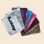 A collection of personalized InchBug sequin pouches in various colors, with one featuring a custom name in black sequins.
