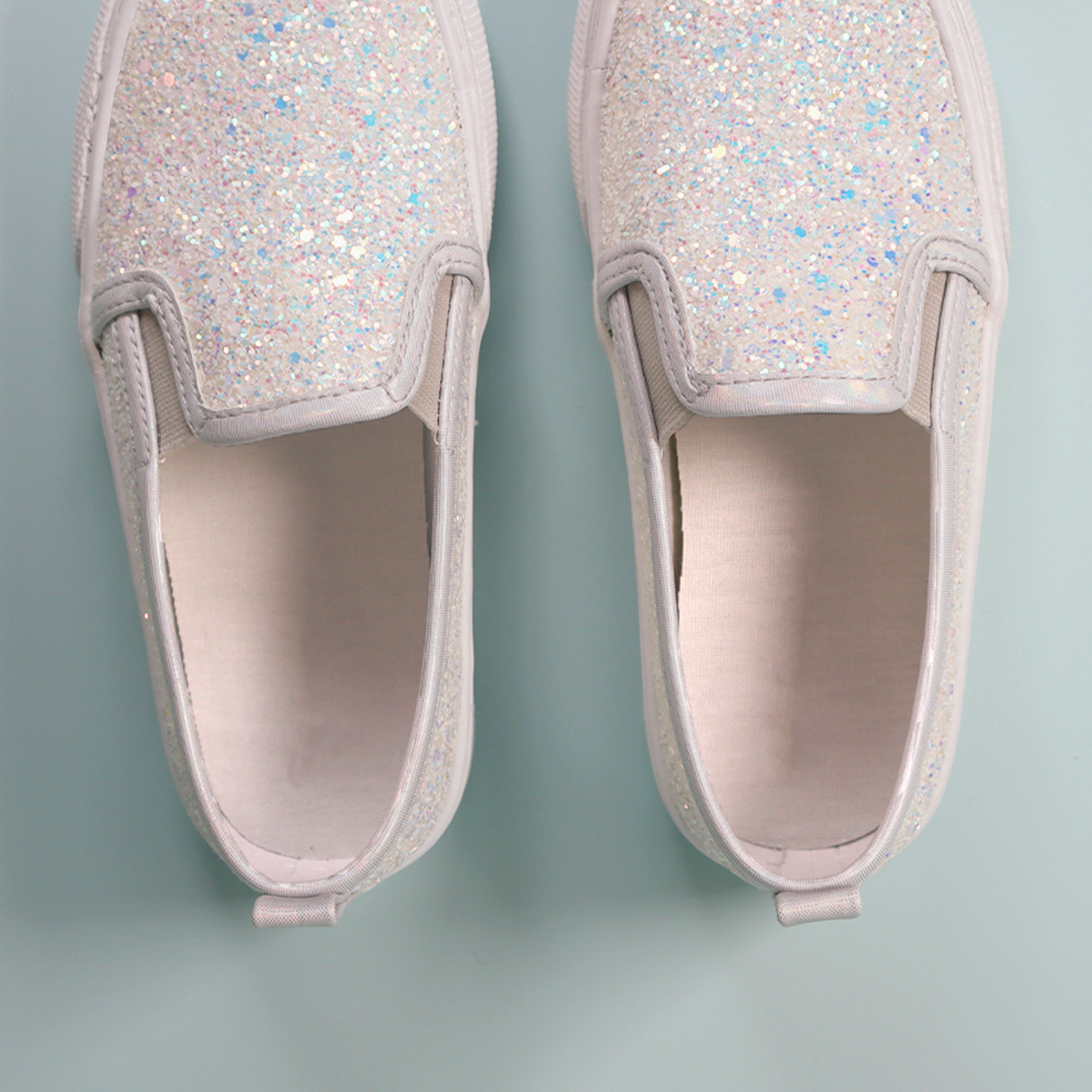 A pair of white sneakers on a two-tone blue background, featuring green InchBug shoe labels attached to the soles.