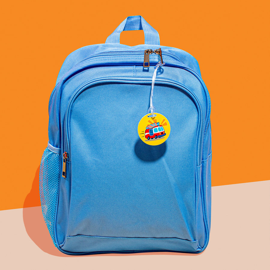 A blue backpack with an InchBug personalized circular kid's bag tag attached to it, placed against a two-tone background