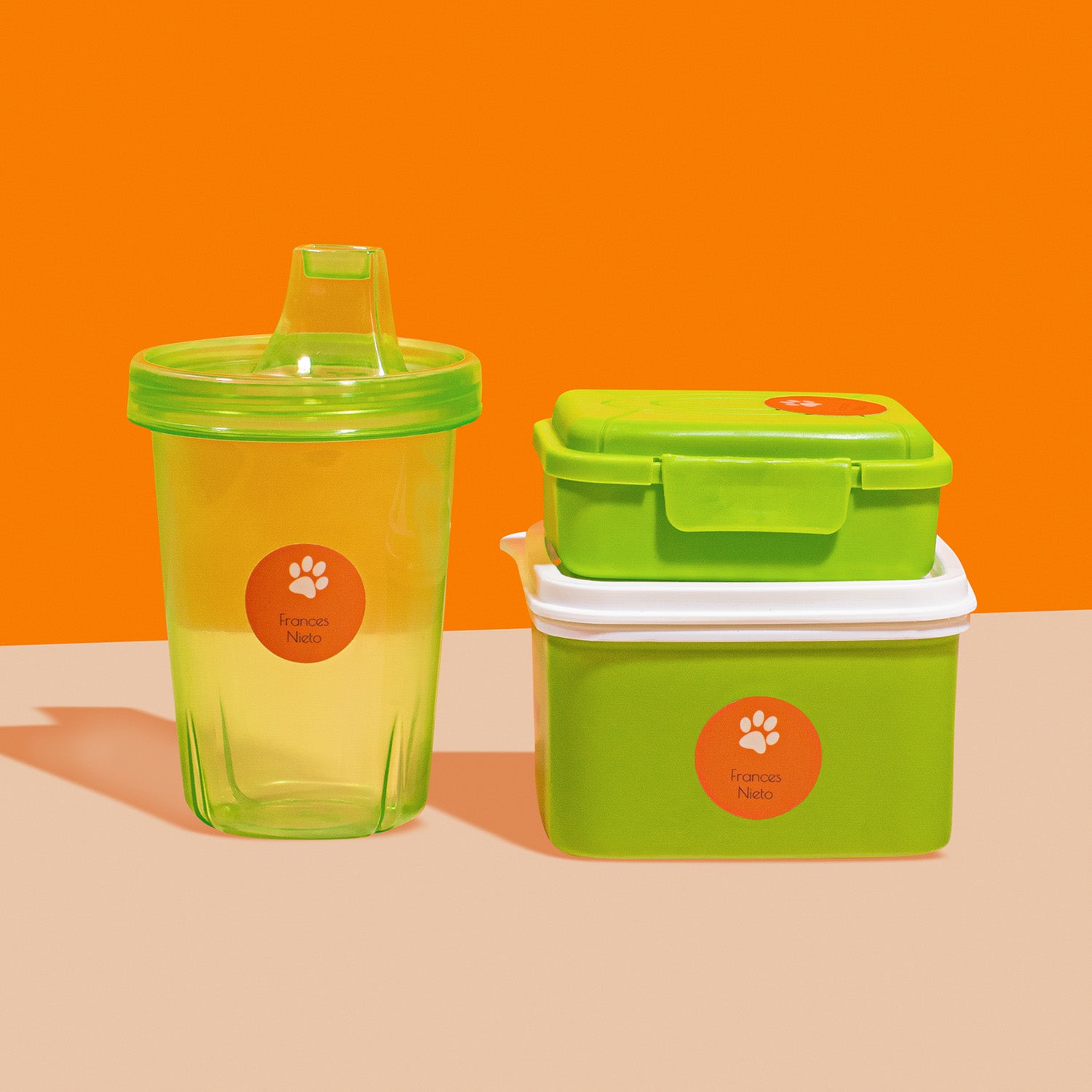 A green sippy cup and a green food container, both featuring personalized InchBug circular name label stickers with a paw print design.