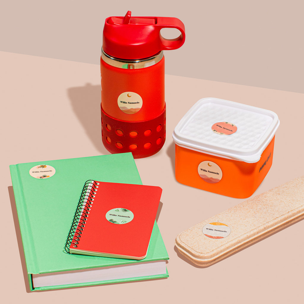 A collection of personal items including a red water bottle, a white and orange container, a green notebook, a red spiral notebook, and a beige book with InchBug circle name labels on them.