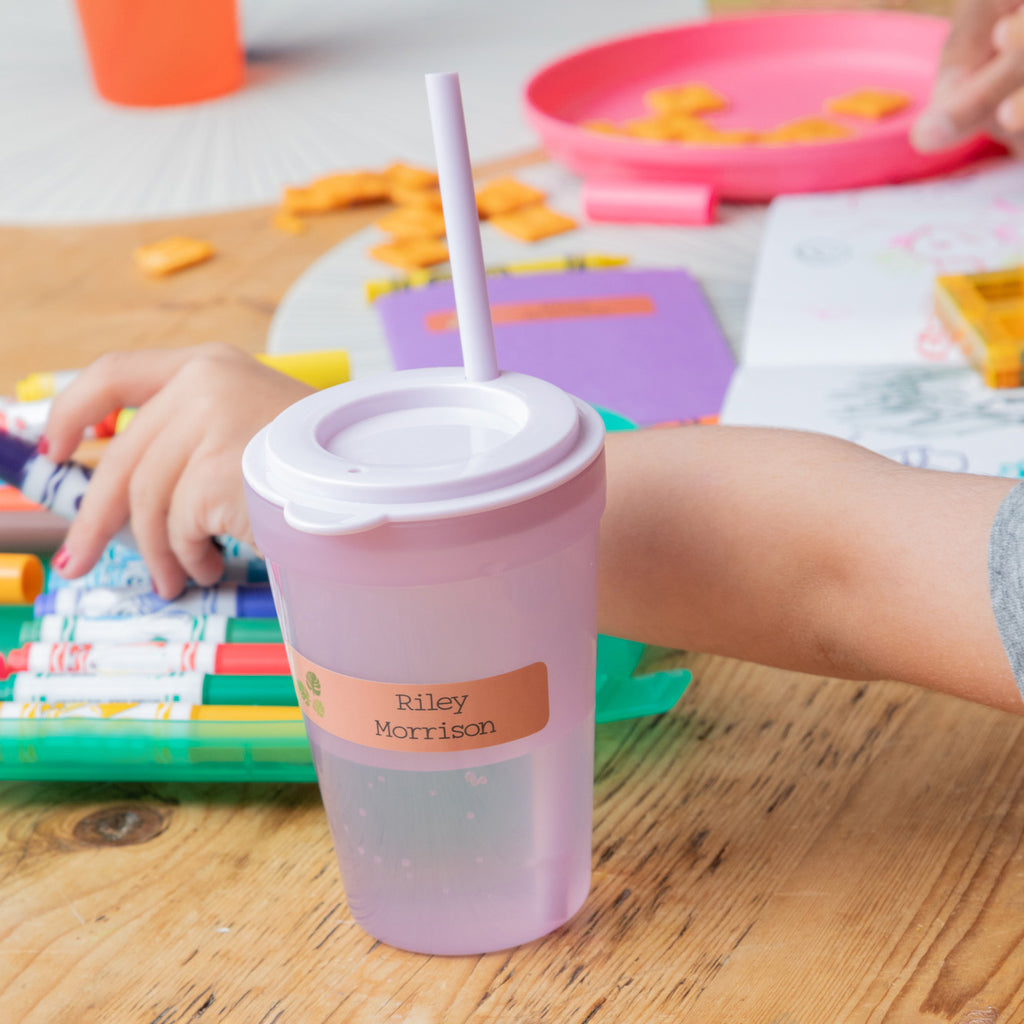 a kid picking a purple colored pen against a pink water cup labeled with InchBug name sticker tag