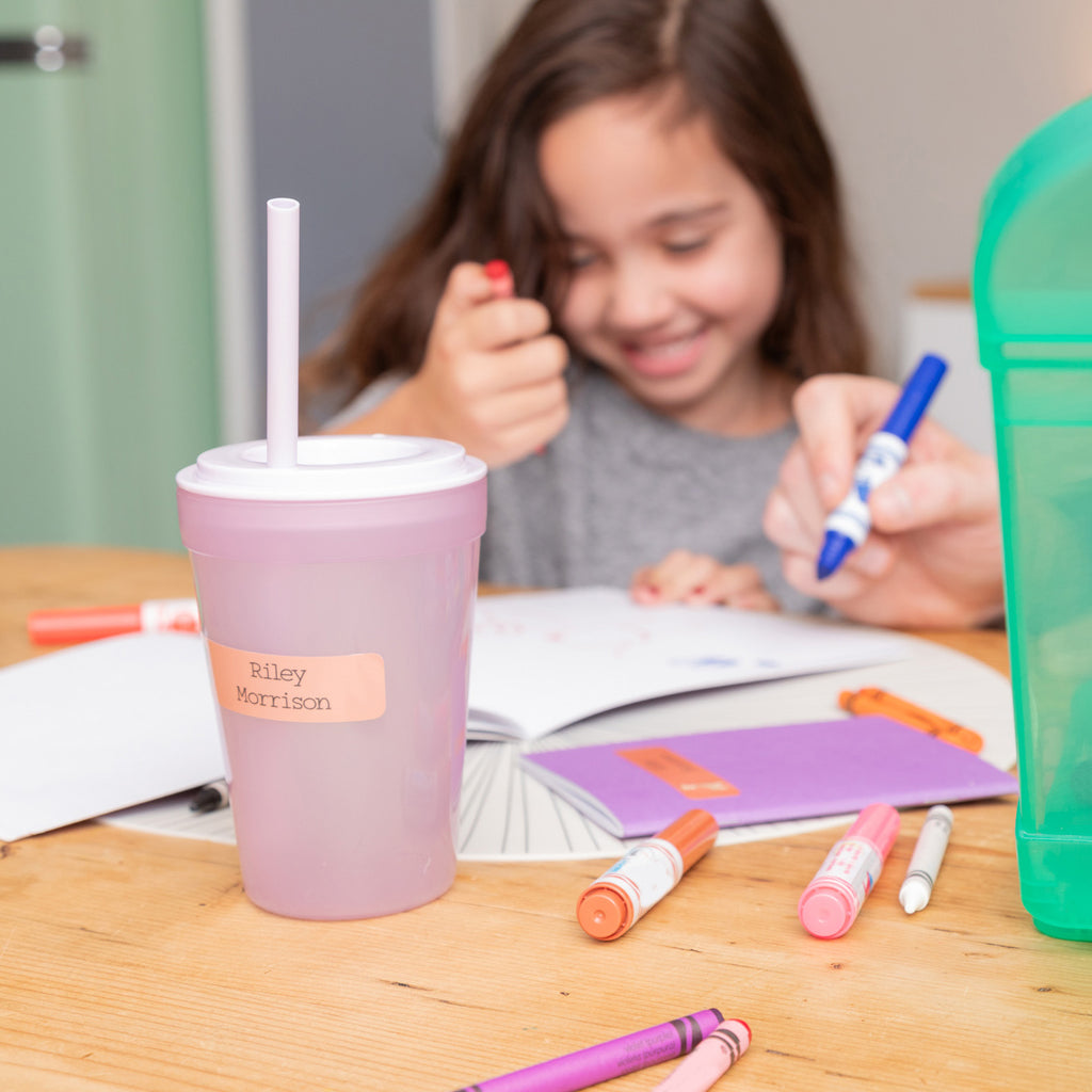 focused photo of a cup labeled with InchBug rectangle label, with a kid doing art behind it