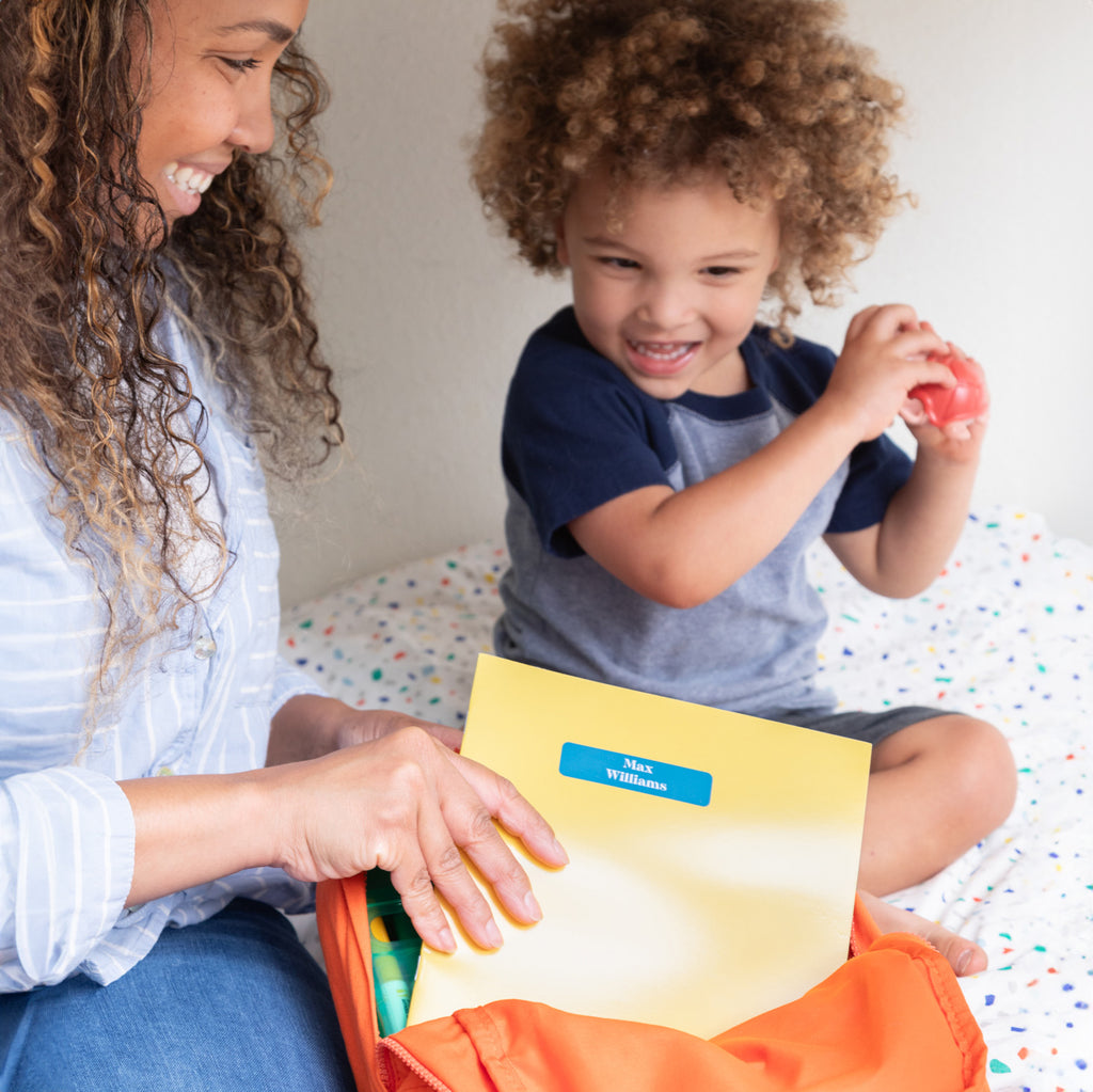 parent and child preparing school supplies; parent is holding a yellow folder with blue InchBug daycare name sticker