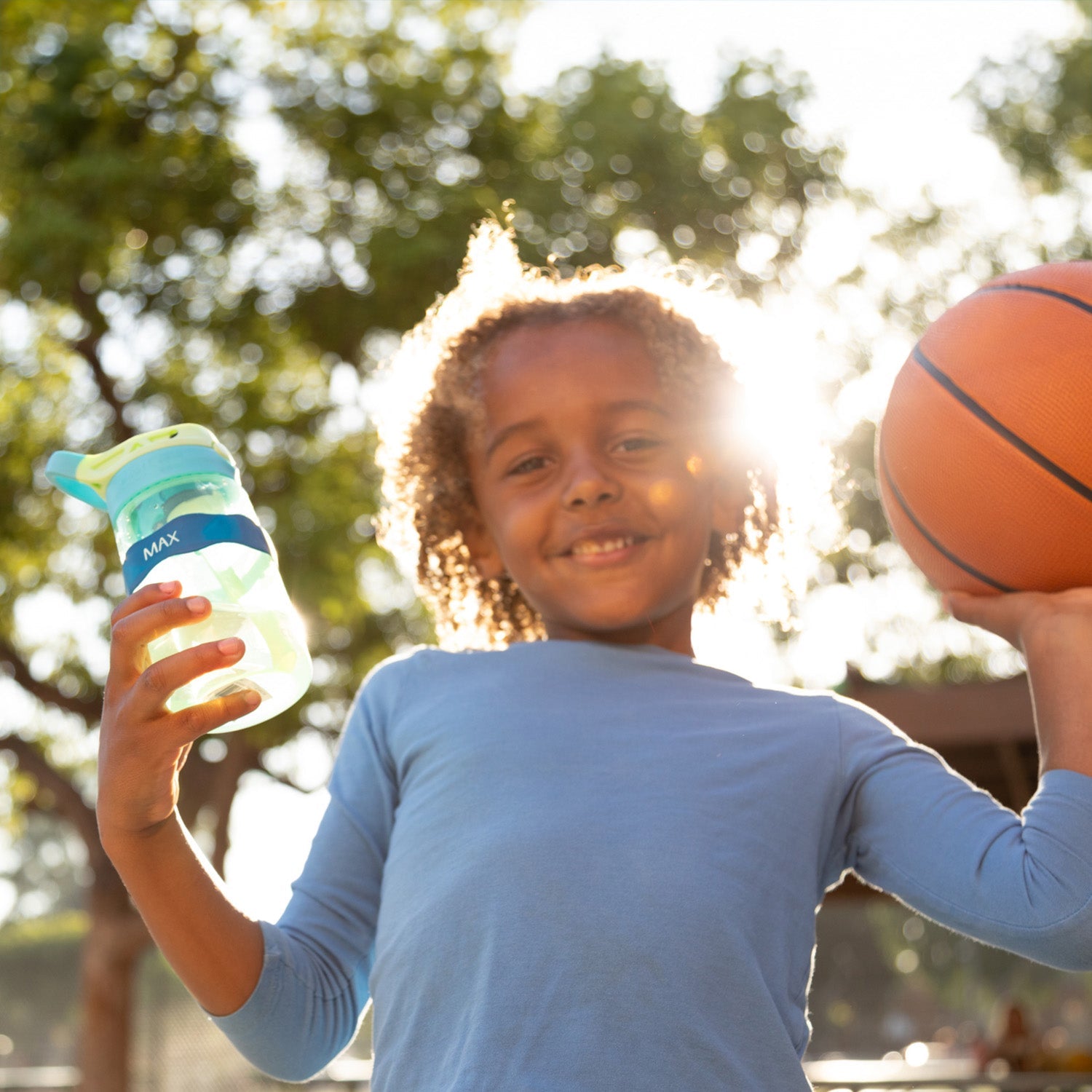 kid holding a water bottle labeled with a blue Orbit Labels® Personalized Water Bottle Label on one hand and a basketball on the other