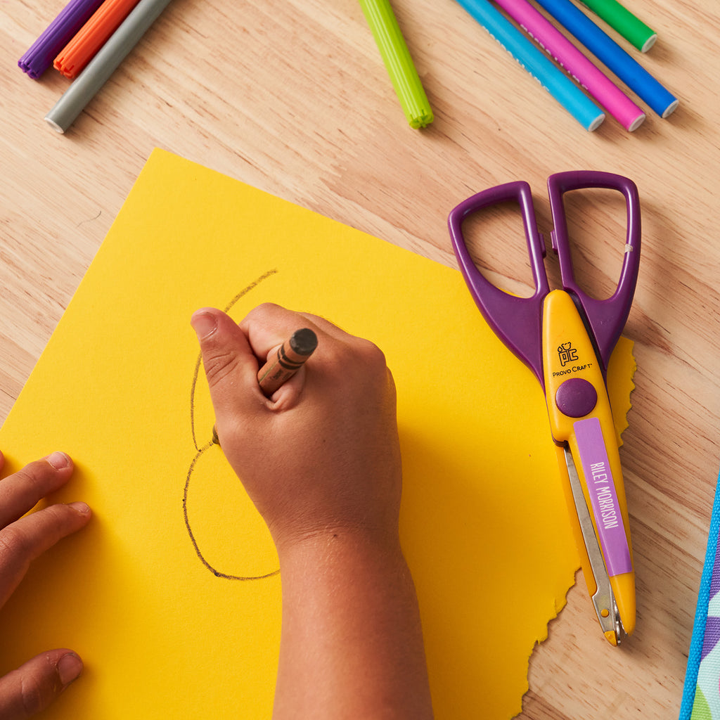 hand of a kid doodling on a yellow paper with a brown crayon