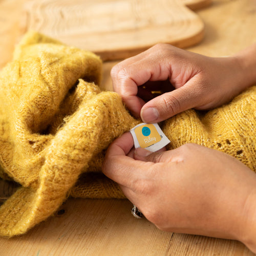 yellow knitted clothing being applied with a yellow InchBug TagPal Kids Clothing Label