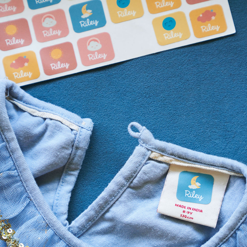 Set of pink, yellow, and blue InchBug TagPal Kids Clothing Labels customized with "Riley", one blue clothes label applied on a blue blouse