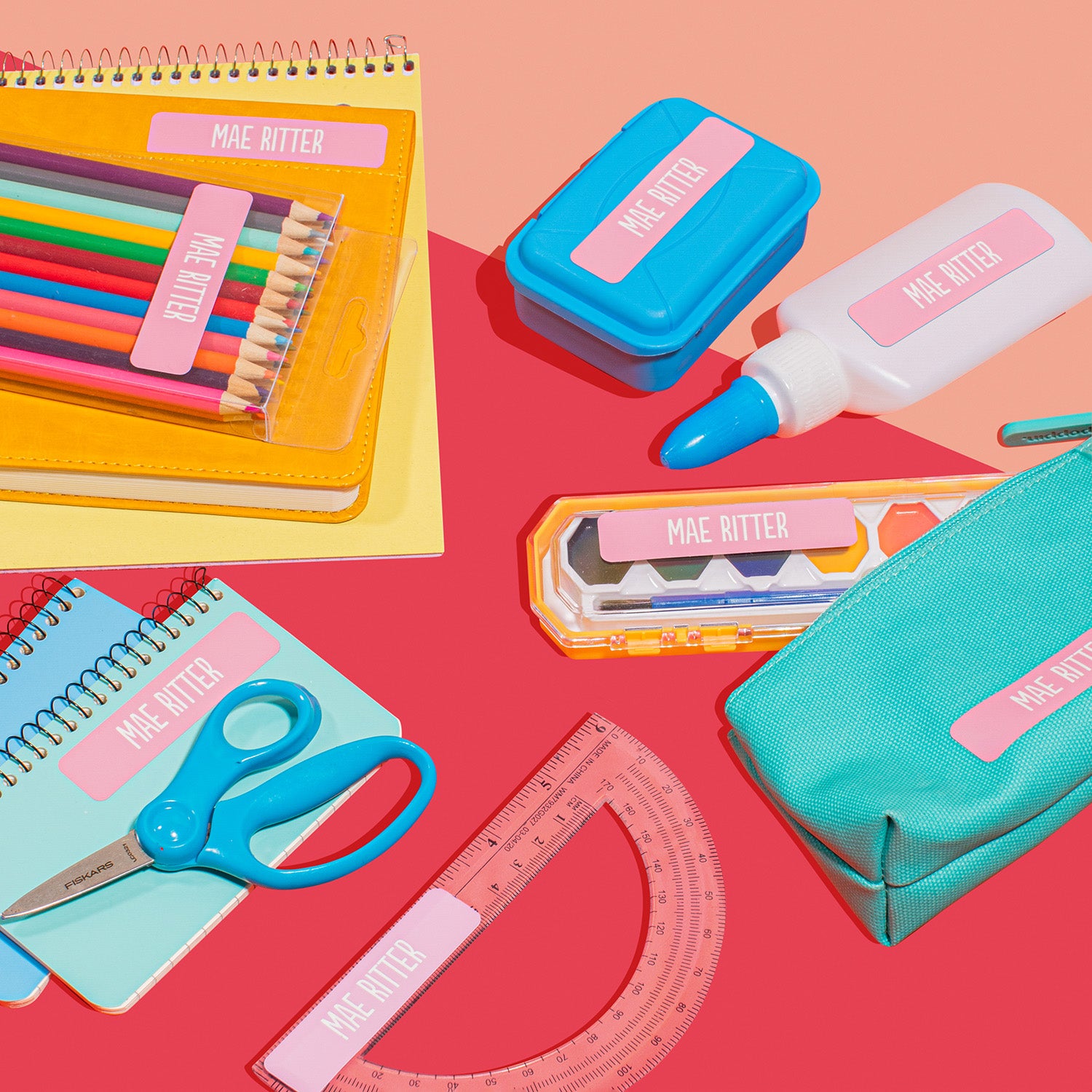A collection of school supplies including colorful pencils, a notebook, a blue container, a pair of scissors, a ruler, and a green pouch, all featuring personalized name labels.