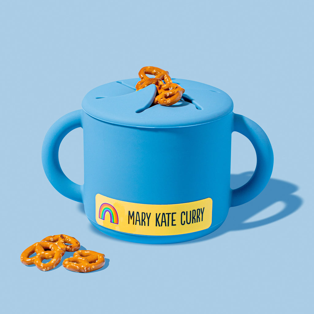 A blue sippy cup with a yellow InchBug sticker name label that reads 'MARY KATE CURRY' and features a small rainbow design.