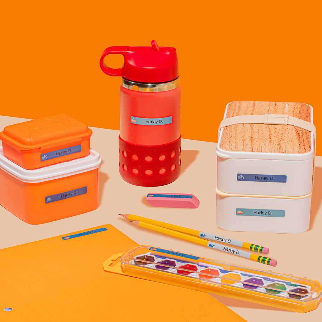 An assortment of personalized InchBug children's labels displayed on various items including a water bottle, lunch box, and school supplies against an orange and white background.