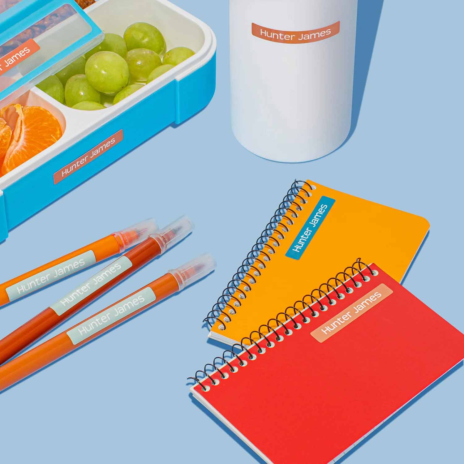 InchBug mini sticker name labels placed on several items, including food container, water bottle, pens, and notebooks