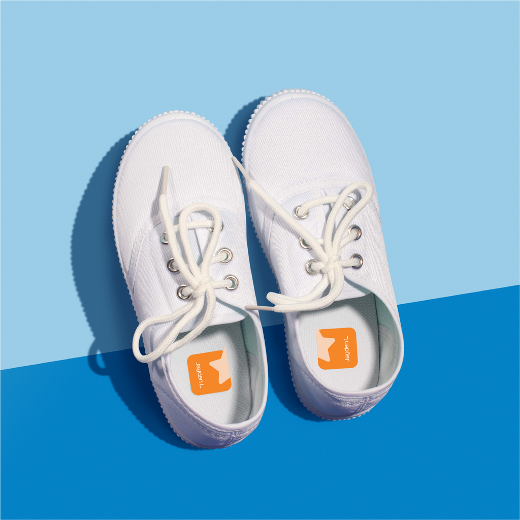 A pair of white shoes with a single orange InchBug ShoePal label attached to one side, displayed against a blue background.