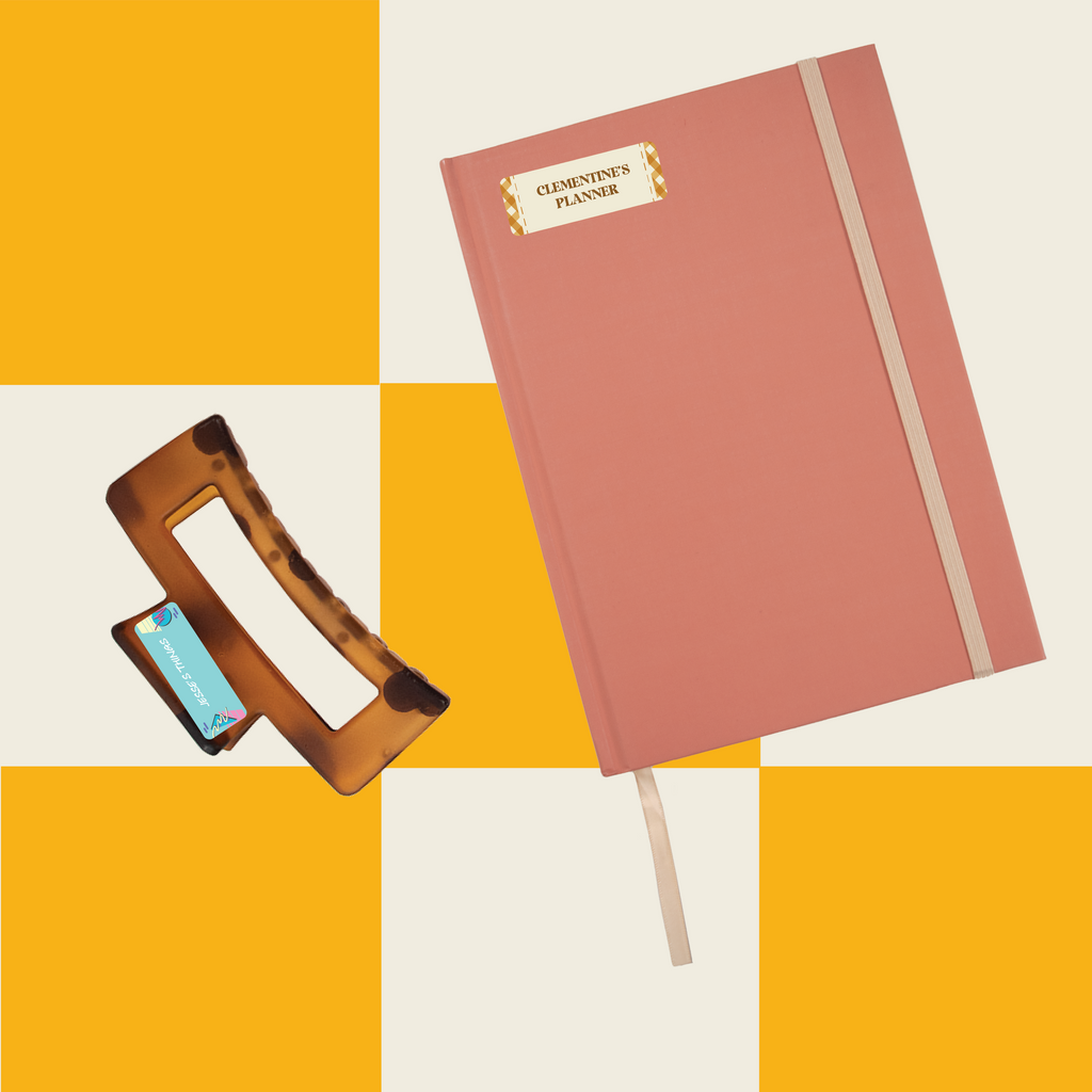 brown hair clamp and pink journal notebook labeled with InchBug sticky name labels, placed against a patterned yellow and white background