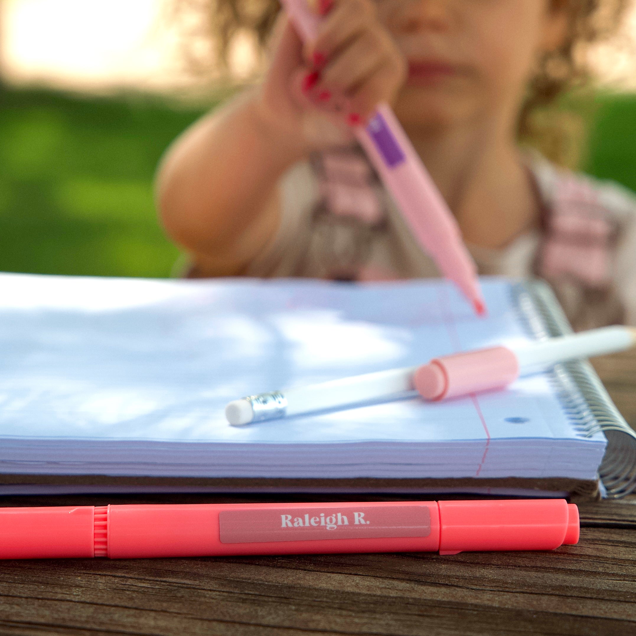 pink pen labeled with pink InchBug label in sharp focus, out of focus is a kid holding another pink pen labeled with purple InchBug label