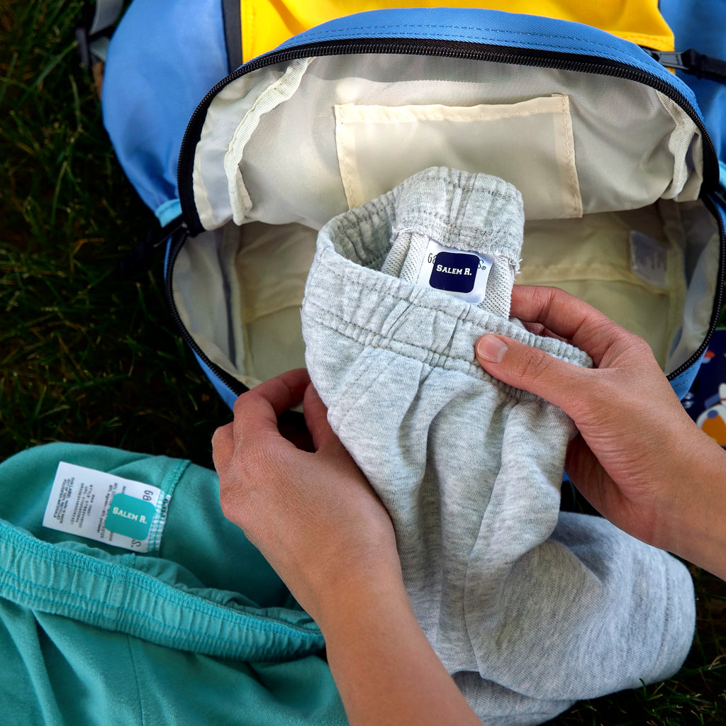 two pairs of shorts being packed, labeled with green and black InchBug TagPal Kids Clothing Labels