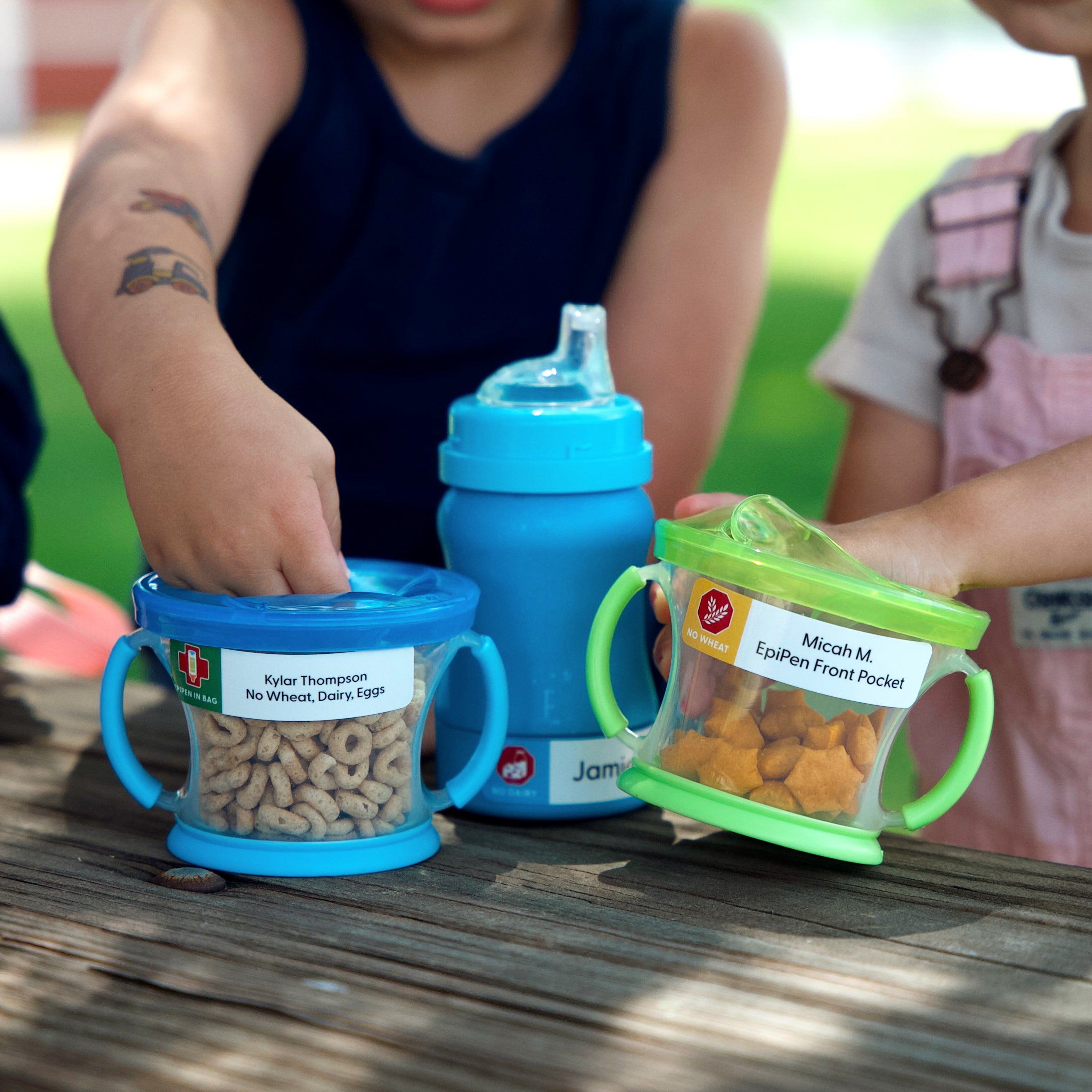 kids holding their snack containers and water bottle, all labeled with InchBug allergy alert stickers with names