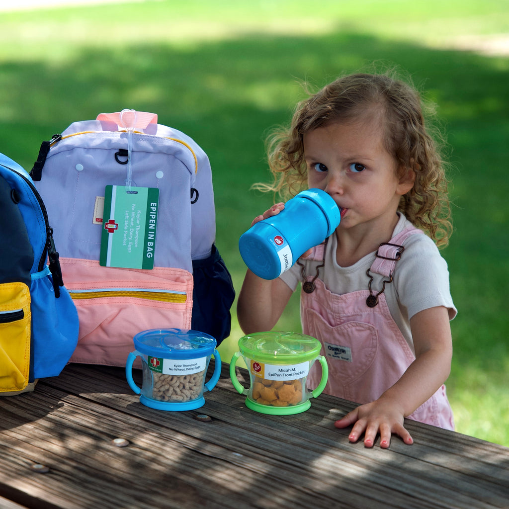 a kid drinking from her blue water bottle labeled with InchBug allergy alert