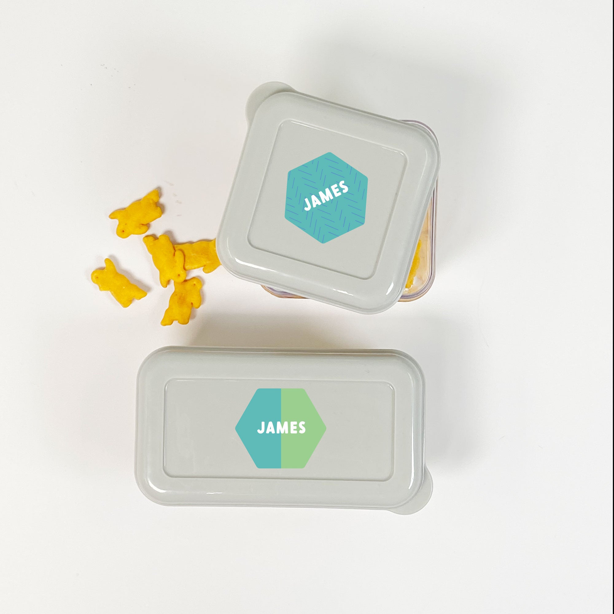 top view of food containers, their grey lids labeled with hexagonal InchBug personalized stickers for kids