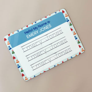 InchBug personalized handwriting board with beanie designs, text reads "EMERY JONES"; placed against a beige background