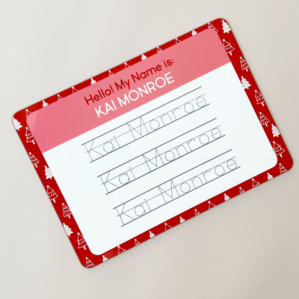 InchBug personalized handwriting board with Christmas tree designs, text reads "KAI MONROE", slanted, placed against a beige background