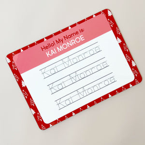 InchBug personalized handwriting board with Christmas tree designs, text reads "KAI MONROE", slanted, placed against a beige background