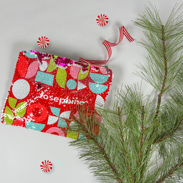 red InchBug personalized sequin pouch designed with various shapes, alongside a pine tree branch