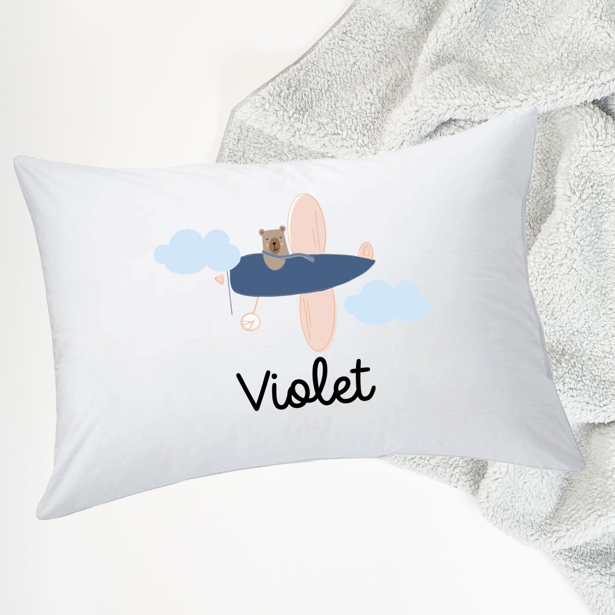 InchBug white pillow with the name 'Violet' printed on it, featuring a design with a bear and clouds, placed on top of a blanket.
