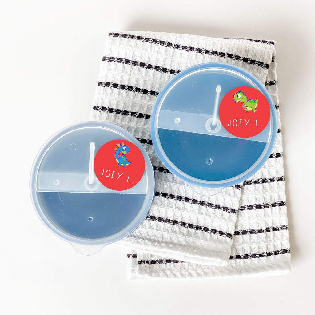 circular red InchBug name sticker labels with dinosaur designs placed on the lids of food containers