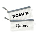 Two grey InchBug personalized zipper pouches with the names 'NOAH P.' and 'Quinn' printed on them.