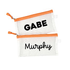 Two orange InchBug personalized zipper pouches with a striped pattern, one labeled 'GABE' and the other with 'Murphy' in bold black lettering on a white background.